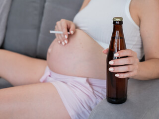 Faceless pregnant woman drinks beer while sitting on the sofa. 