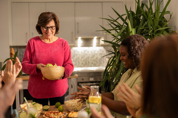 Senior woman bringing food to the table at a gathering of diverse cultural friends