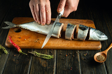 Slicing raw mackerel fish on a kitchen board with a knife in the chef's hand before salting with...