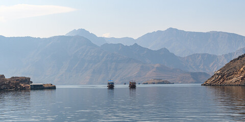 Two boats gently sail through the serene waters of Khasab’s fjords, surrounded by the majestic...