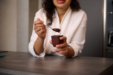 Focus on woman's hands, holding a teaspoon and a container with wholesome chocolate vegetarian...