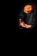 Skillful chef in black attire tossing a garnished burger in the air, captured against a dark background. A dynamic display of culinary expertise and appetizing food.