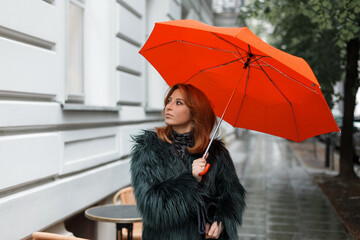 Fashion beautiful girl in stylish clothes with a bright orange umbrella walks in the city on a rainy day