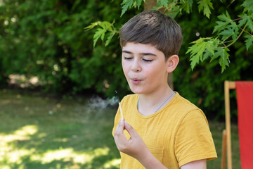 Fototapeta premium Little naughty boy holds burning match in hands and plays with fire on the backyard 
