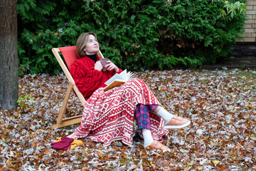 A woman sits on a bench on the backyard as she gets lost in the pages of her book. The autumn...