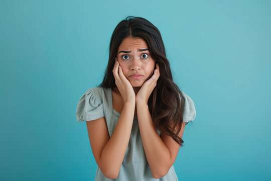 Nervous Latin woman in studio with oops reaction to gossip on blue background. Mistake, sorry and female overwhelmed by fake news