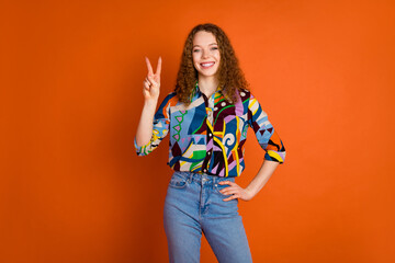 Photo of lovely cheerful nice girl wear stylish print clothes demonstrate v-sign isolated on vivid orange color background