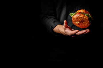 Skillful chef in black attire tossing a garnished burger in the air, captured against a dark background. A dynamic display of culinary expertise and appetizing food.