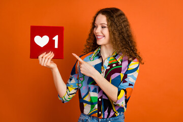 Photo of charming adorable girl blogger wear trendy print clothes hands hold red heart symbol isolated on vivid orange color background