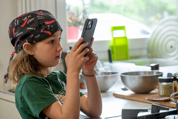 Girl in chef's hat filming father cooking with mobile phone for social media