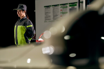 A female employee at a gas station is directing cars to stop for refueling