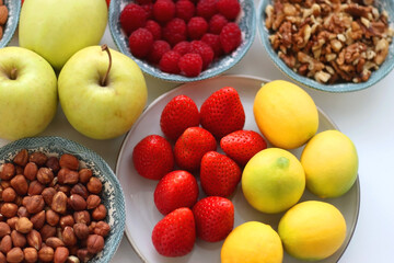 Apples, lemons, bananas, berries, carrots, leek, tomatoes, radishes, spinach and various nuts on white background. Healthy seasonal fruit and vegetable. Selective focus.
