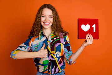 Photo of pretty adorable girl wear stylish print clothes thumb up heart symbol isolated on vivid orange color background
