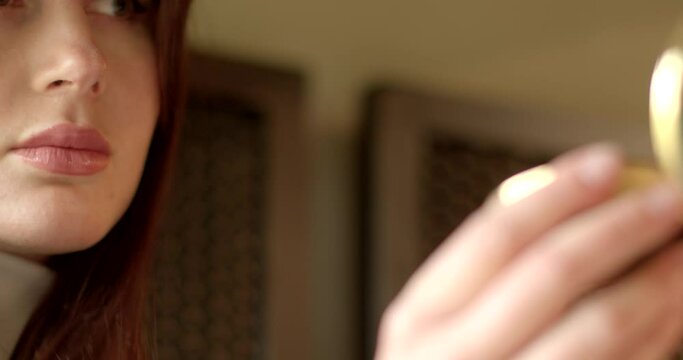 Young woman gazes into a small mirror, anticipation dating in her eyes as she prepares for a romantic rendezvous with her partner. Close-up girls face before dating.