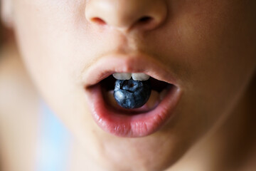 Anonymous teenage girl holding organic blueberry between teeth