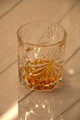 An expensive crystal glass with a light colored brown shot of liquor sitting on a marble countertop.