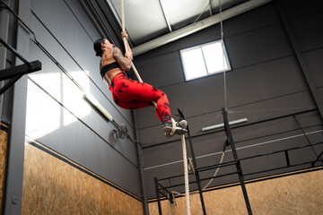 Woman training climbing a rope in a cross training center - 796508539