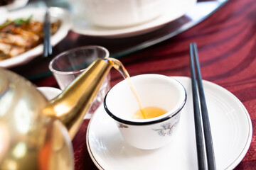 Pour natural chamomile tea from the teapot into the cup on the tableware