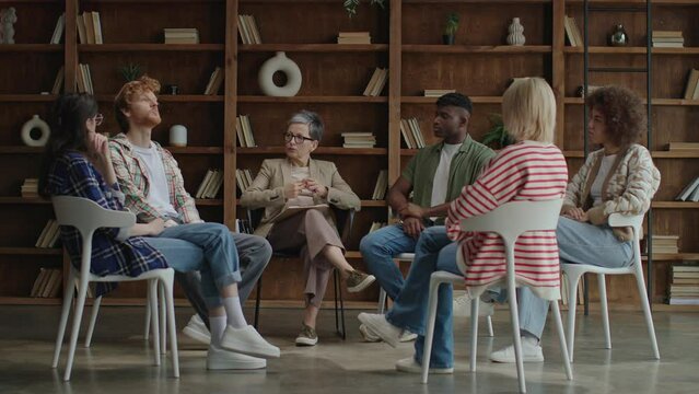 In a contemporary setting, six diverse young adults convene in a circle for a therapeutic session, fostering growth and solidarity