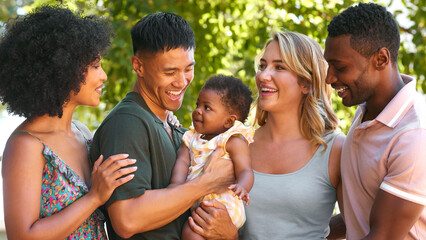 Portrait Of Multi-Racial Family And Friends Hugging Baby Outdoors  In Countryside In Group Together