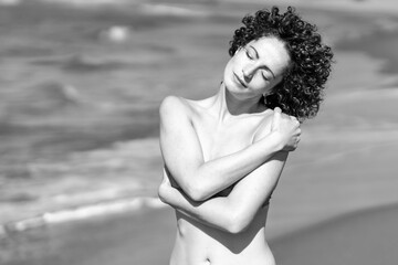 Slim woman in bikini standing on knees on sandy beach