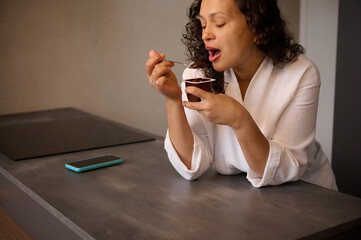 Young woman eating tasty yoghurt in the home kitchen
