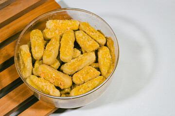 Long cheese and nut cookies are served in round packaging with a plain white background and on a wooden coaster