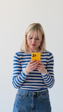 Serious and focused Caucasian woman using smartphone on white background. Texting online or browsing internet concept. Vertical video.