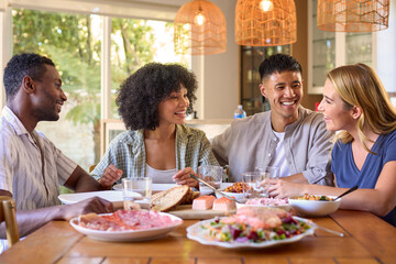 Group Of Multi-Racial Friends Sitting Around Table Enjoying Meal At Home Together