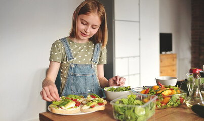 Girl preparing sandwiches with avocado, tomatoes cherry and arugula at kitchen. Vegetarian bruschettas and salad with fresh vegetables and greens