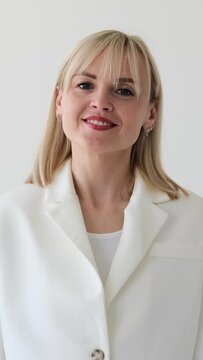 Close up portrait of a happy and smiling Caucasian female employee, director or entrepreneur, standing on white background. Vertical video.