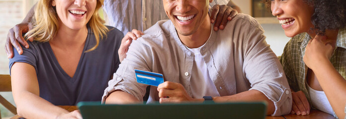 Close Up Of Multi-Cultural Group Of Friends With Laptop And Credit Card Booking Holiday Online