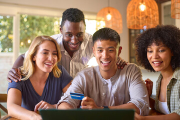 Multi-Cultural Group Of Friends With Laptop And Credit Card Booking Holiday Or Shopping Online