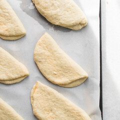 Coco bread dough rising on a parchment lined baking tray, shaped coco bread about to be baked, process of making jamaican coco bread