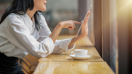 Engaged businesswoman using a digital tablet in a cozy coffee shop setting with a fresh cup of coffee on the table.