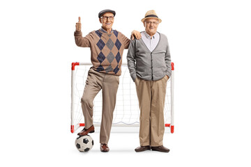 Elderly men standing with a football in front of a goal and gesturing thumbs up