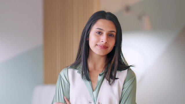 Portrait of young confident happy Indian business woman in corporate office. Smiling businesswoman or student, professional employee, female entrepreneur standing arms crossed looking at camera.