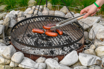 Obracać kiełbasę na grillu, mięso leży na ruszcie nad gorącym żarem