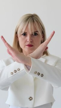 Serious portrait of a concentrated woman showing stop sign with crossed arms on white background. Disagreement, restriction, protection concept. Vertical video.