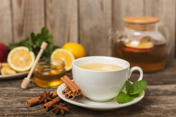 Fragrant hot tea with cinnamon stick and anise on a textured wooden background. A cup of hot tea with honey, lemon, mint and apples. Spicy tea with spices. Immunity tea. Health concept.Copy space.