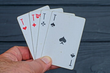 four white playing cards with paper aces hearts spades diamond and cross in hand on the background of a black wooden table