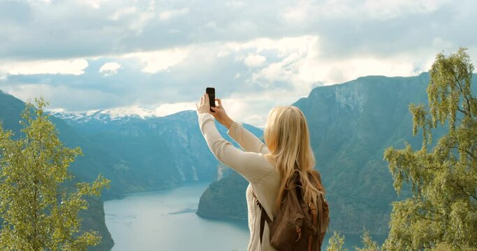 Woman, back and phone for mountain photography, view and travel blog by Norway lake. Tourist, person and mobile technology for holiday, vacation and hiking review of nature picture for social media