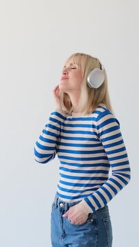 Satisfied and carefree Caucasian woman listening music in wireless headphones, relaxing during leisure time on white background. Vertical video.
