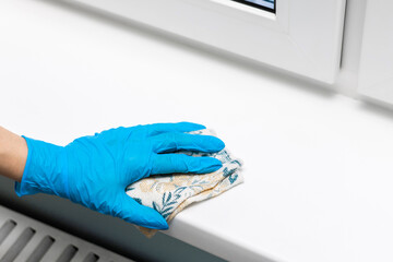 housewife wearing gloves wipes a plastic window sill.
