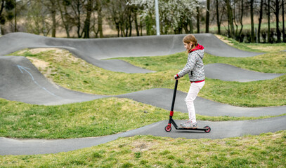 Beautiful little girl rides a scooter in a extreme ride park