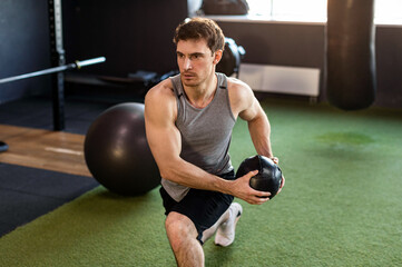 Young strong man exercising with medicine ball in gym, having morning workout
