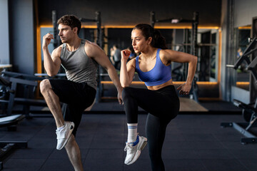 Active couple doing elbow-knee warm up exercises during fitness workout in modern gym