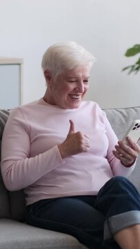 Surprised Caucasian mature woman using smartphone, receiving good news and exclaiming wow at home living room. Happy online retirement. Vertical video.