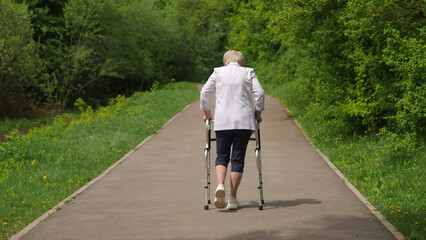 Elderly woman strolling with walker on path lined with trees and grass