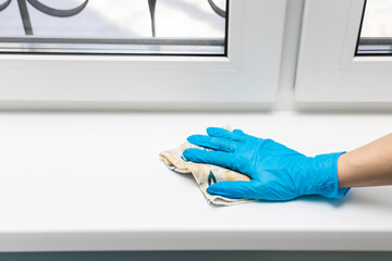 housewife wearing gloves wipes a plastic window sill.